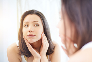 woman looking at her face in mirror after using retinol